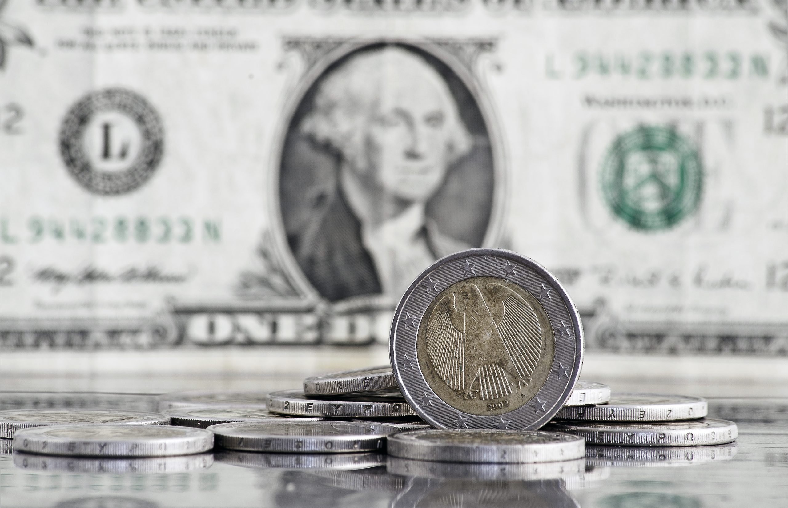 image of Euro coins in front of a blurred Dollar note in the background